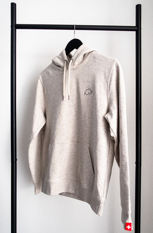 Weiss-natürlicher unisex Twelvetia Pullover mit schwarz gestickter Schweizer Landesumrandung auf linker Brust und Schweizer-Flagge-Etikett am linken Ärmel. Hängend an schwarzem Bügel vor weisser Wand.