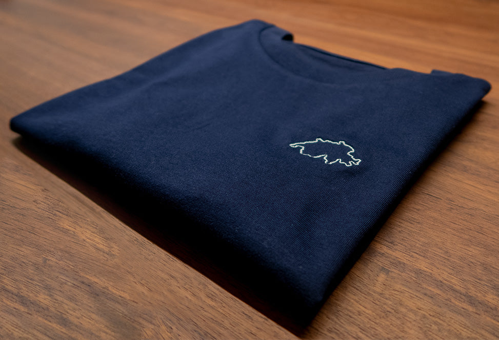 Navy-blaues Twelvetia T-Shirt für Frauen mit weiss-gestickter Schweizer Landesumrandung gefaltet auf holzfarbenen Tisch liegend