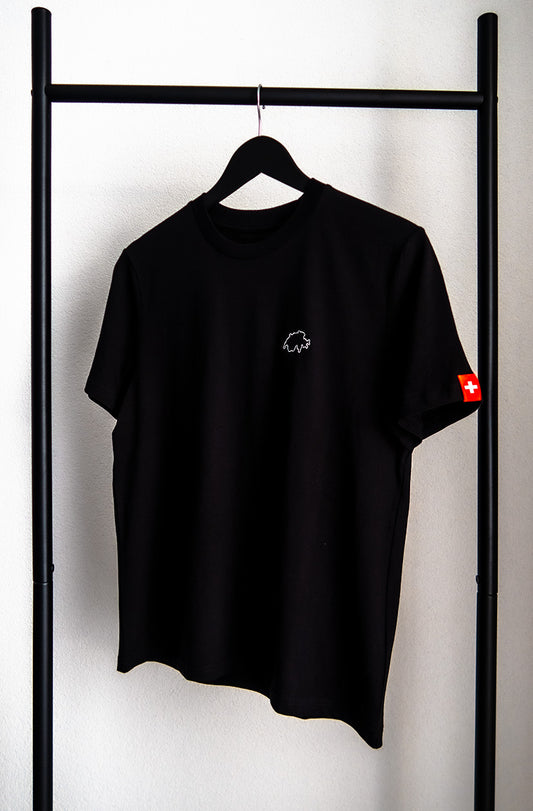 Schwarzes unisex Twelvetia T-Shirt mit weiss gestickter Schweizer Landesumrandung auf linker Brust und Schweizer-Flagge-Etikett am linken Ärmel. Hängend an schwarzem Bügel vor weisser Wand.